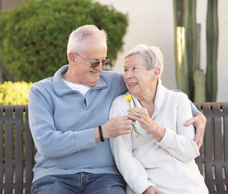 Elderly husband handing yellow daisy to wife