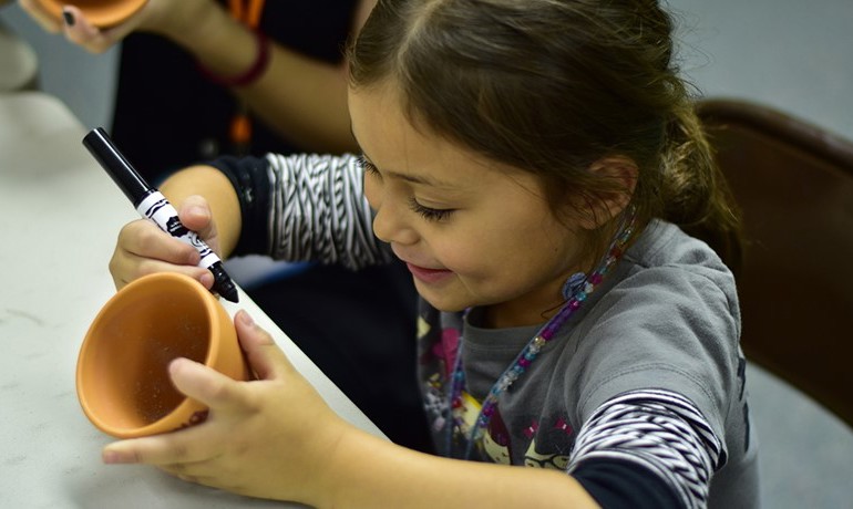 Girl decorating a ceramic cup with a marker
