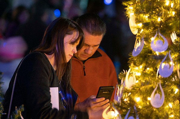 Two attendees look at a photo together near a Christmas tree