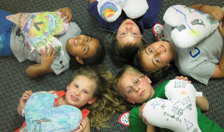 New Song children lying in a circle holding decorated heart ballons