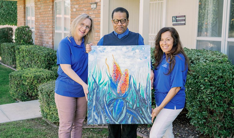 Artist Artino Sims, nurse Lisa Schultz, and social worker Mica Dalley pose with a painting by Artino