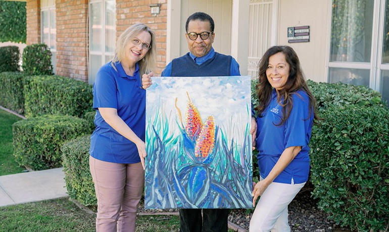 Artist Artino Sims, nurse Lisa Schultz, and social worker Mica Dalley pose with a painting by Artino