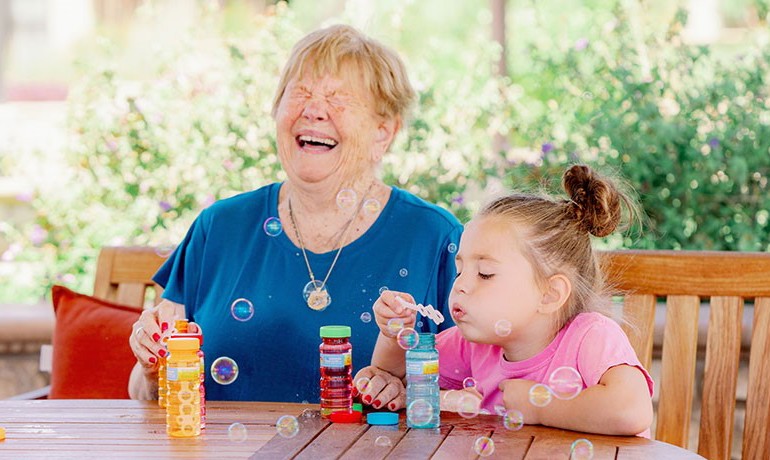 Child blows bubbles while older woman laughs