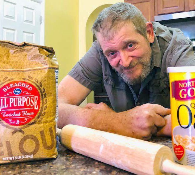 Baker leaning on counter behind bag of flour and rolling pin