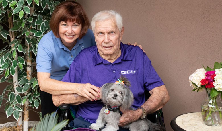 Diane Bykowski standing behind Bruce Moses seated and holding therapy dog Mia