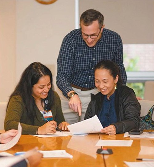 Dr. Ned Stolzberg standing between Prachi Aggar­wal and Kristina Balangue seated at table